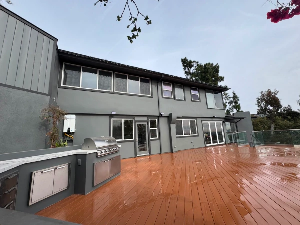 Gray painted hillside home with a stained wood deck and outdoor kitchen